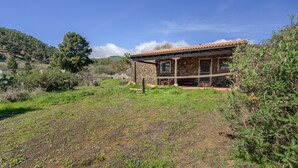 Una casa de piedra con techo de tejas, rodeada de un campo cubierto de hierba y árboles.