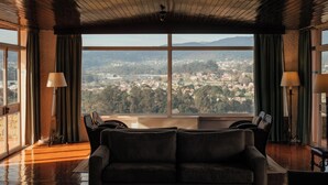 Habitación con un ventanal grande que ofrece vistas a un paisaje urbano y montañas. Se puede ver un sofá y dos lámparas.