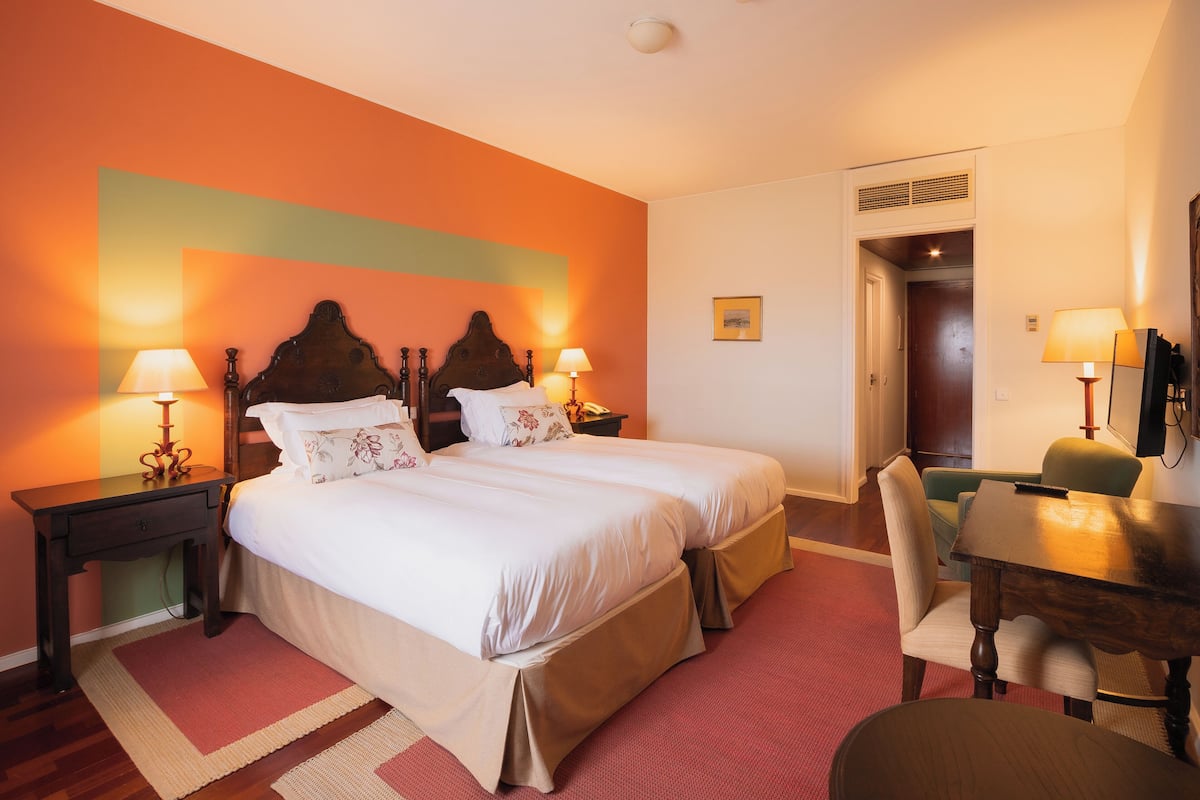 A hotel room with two beds, a desk, and a chair.