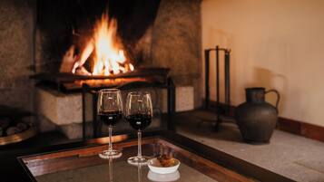 Una chimenea con fuego, dos copas de vino, un cuenco pequeño y una jarra sobre una mesa.