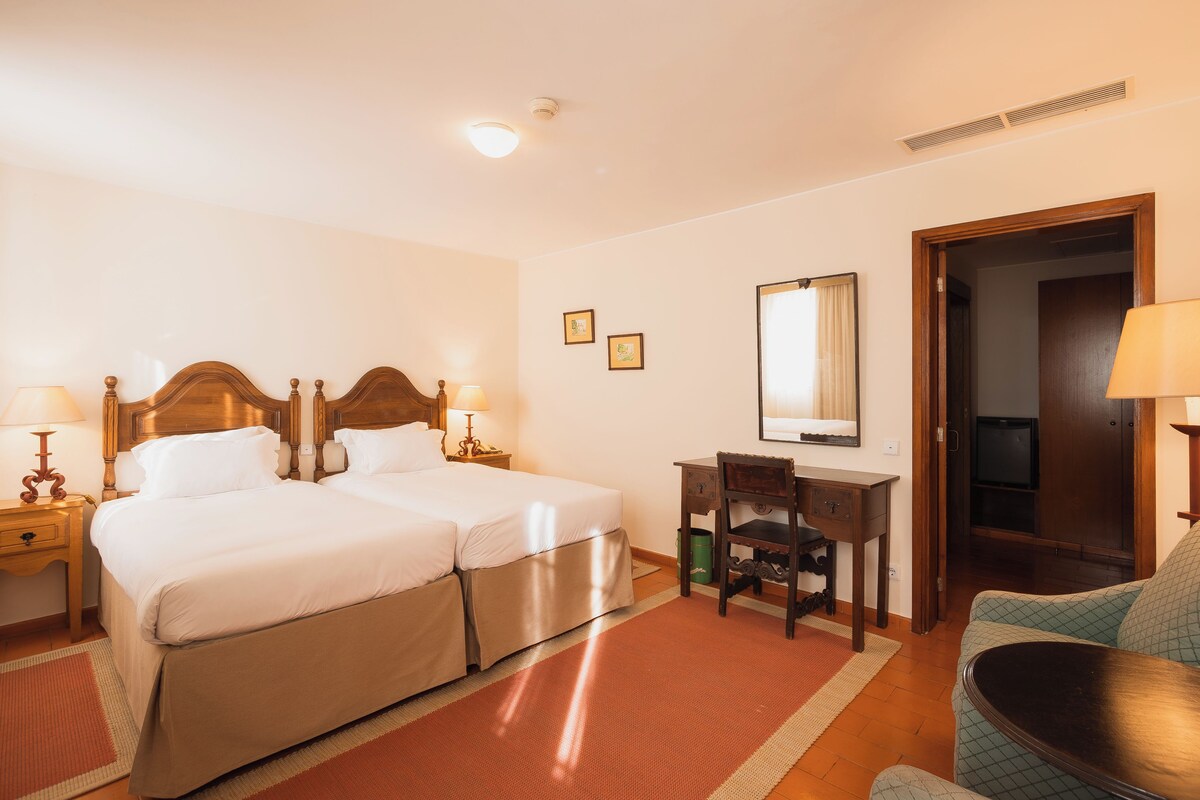 Een hotelkamer met een tweepersoonsbed, een bureau met stoel, een televisie en een lamp.
