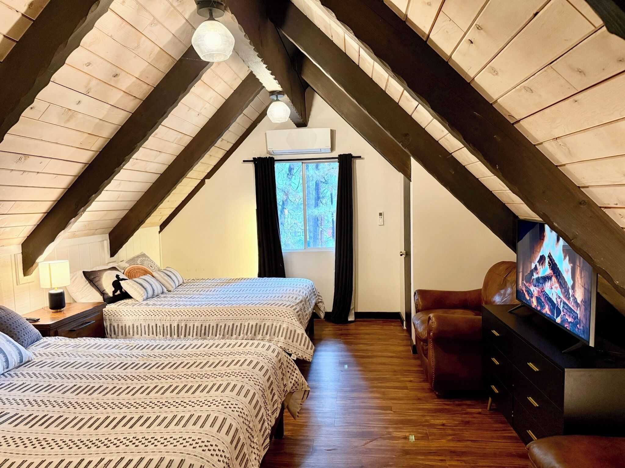 A cozy attic bedroom with two beds, a TV, and a fireplace.