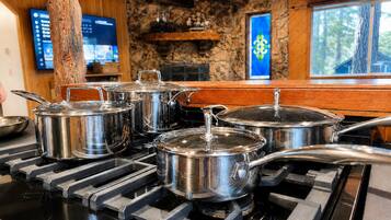 A kitchen with stainless steel pots on a gas stove, a wooden interior, stone walls, and a window with a view of trees.