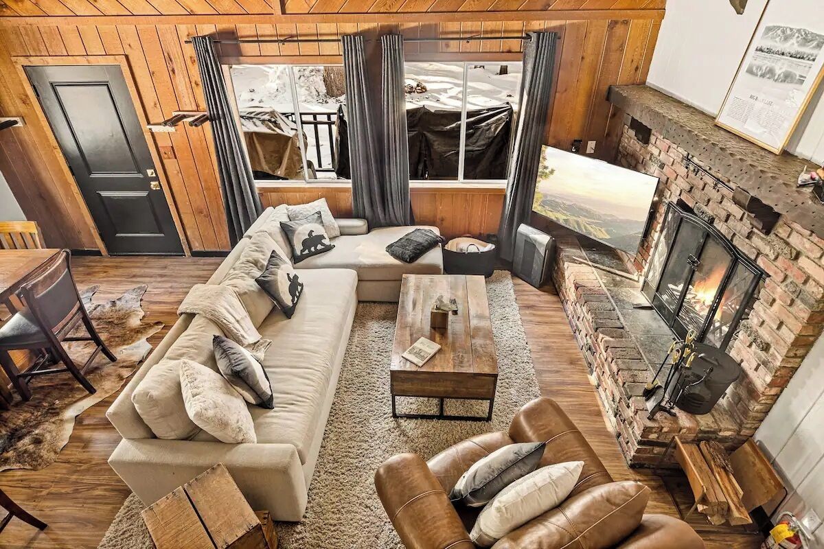 A cozy living room with a sofa, leather armchair, fireplace, and a view of the outdoors.