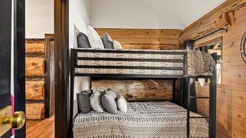 Un lit superposé avec une literie et des oreillers à motifs, placé contre un mur fait de rondins de bois.