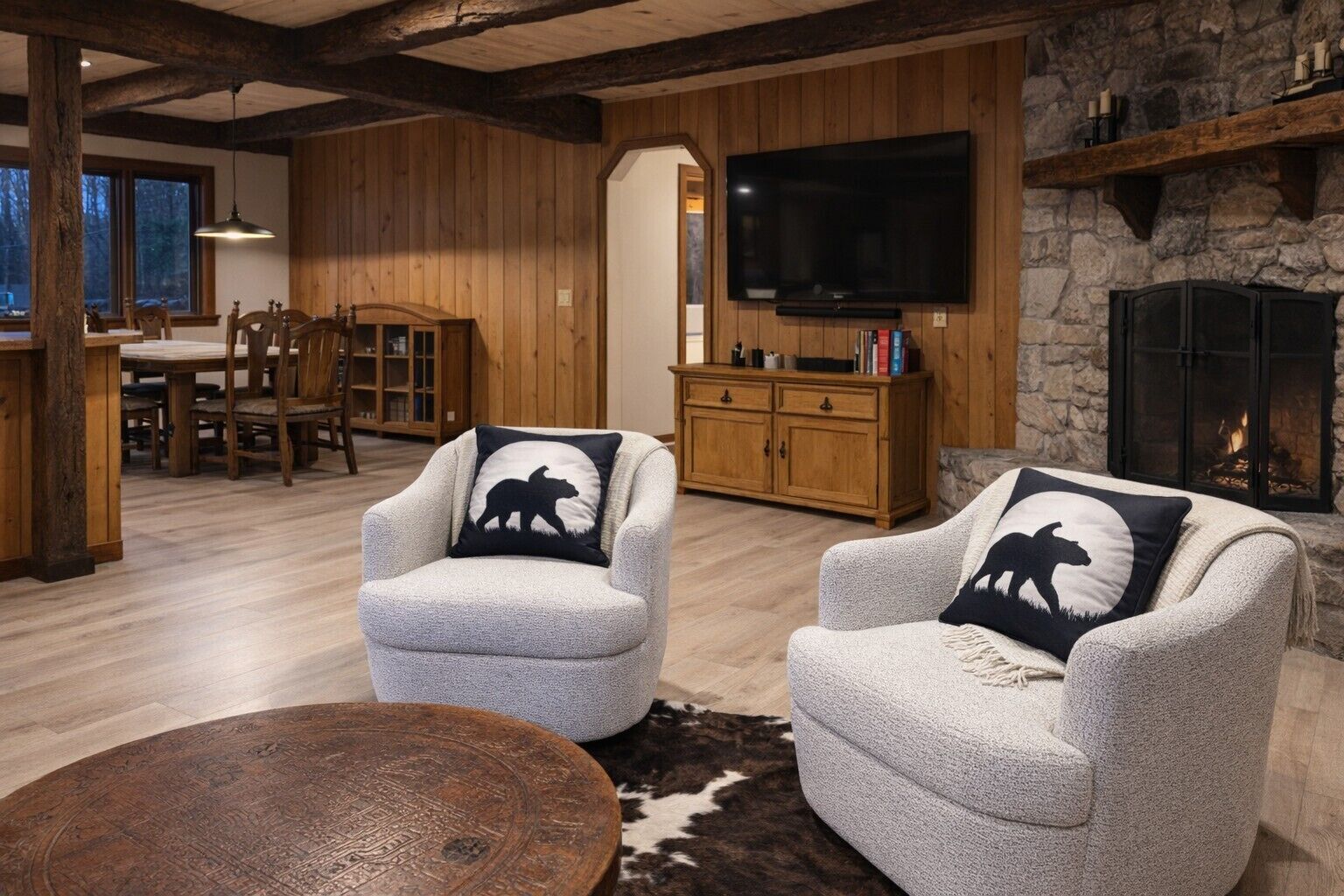 A cozy living room with two armchairs, a wooden dining table, a fireplace, and a TV.