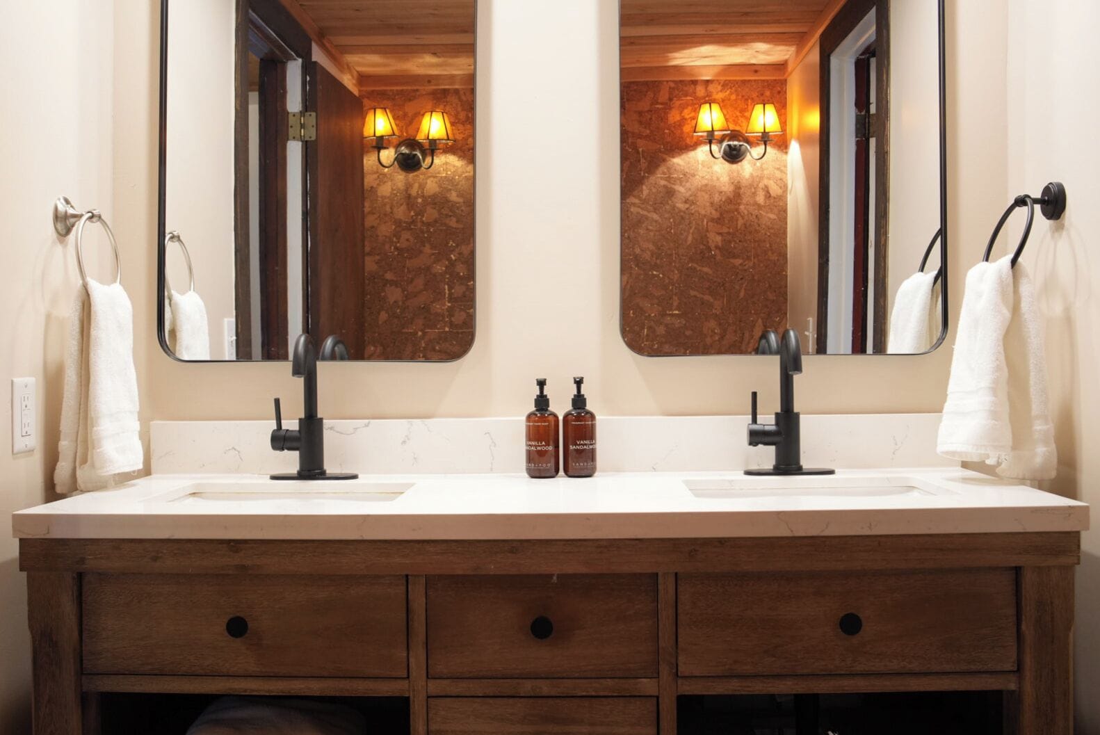 A bathroom with two sinks, wooden cabinets, and a large mirror with wall sconces.
