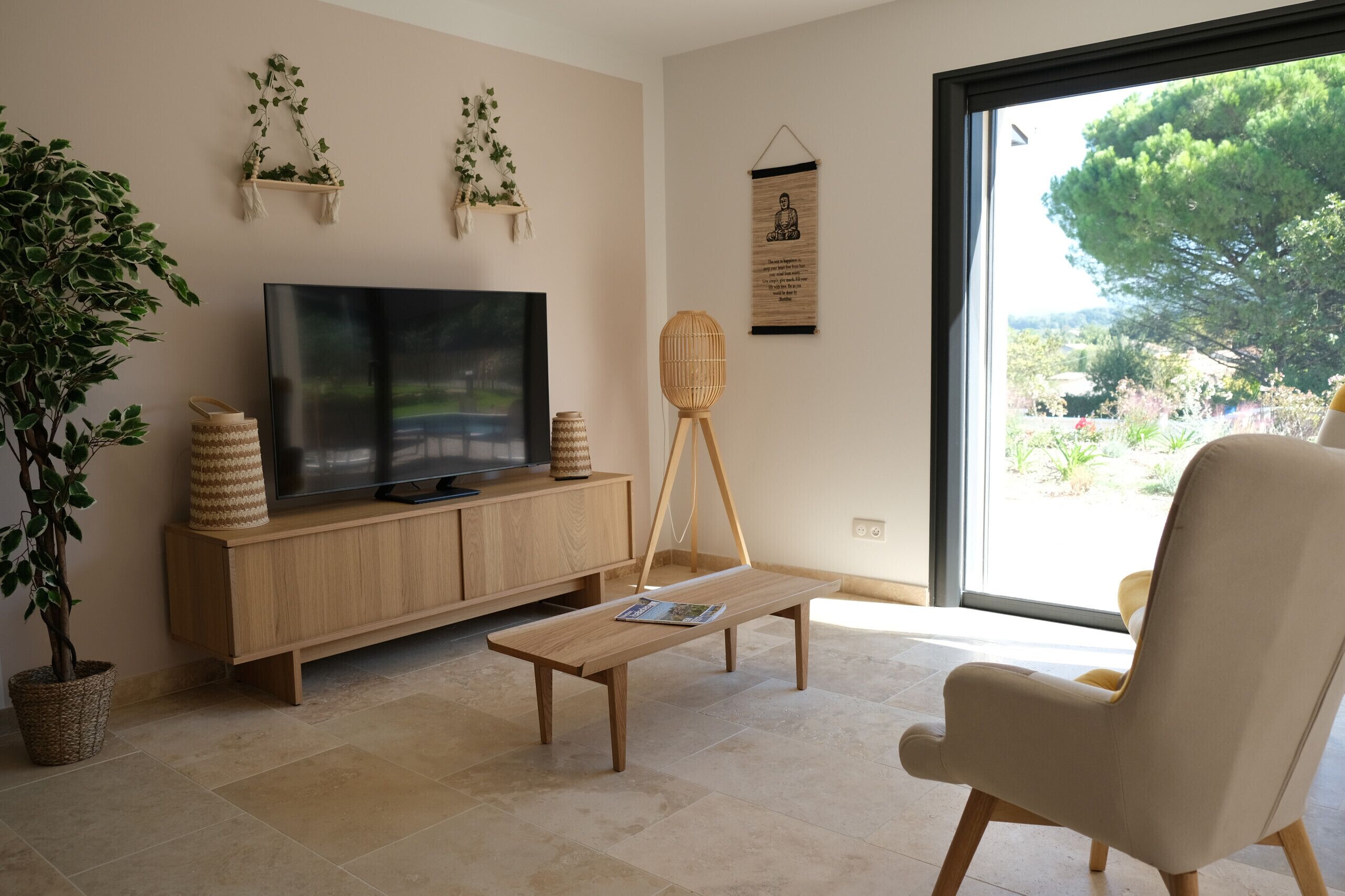 Un salon avec un téléviseur, des meubles en bois, une plante et une vue sur l’extérieur.
