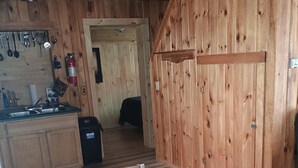 A wooden interior with a dining table, kitchen area with utensils, and a bed in the background. - Rustic  cabin  in Lincoln Maine  (Lincoln)