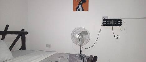 A bedroom with a bed, a wall-mounted fan, and a power outlet.