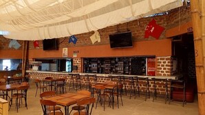 A spacious bar area with multiple seating options, a counter with a menu, and a brick wall backdrop. - Zuri Resort Bungoma (Bungoma)