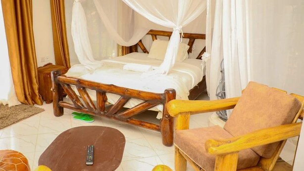 A room with a bed, a wooden chair, a remote control, and a small table. - Zuri Resort Bungoma (Bungoma)