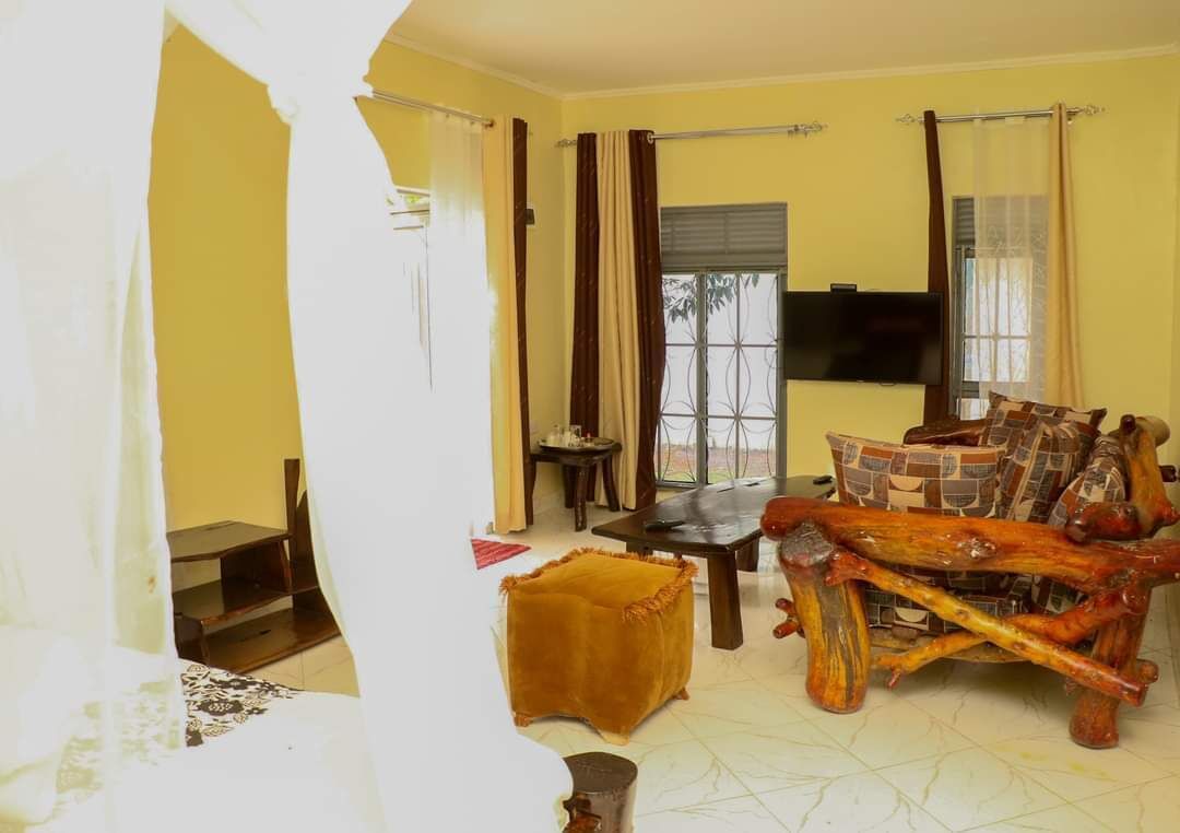 Un salon comprenant un canapé, une table basse et un téléviseur fixé au mur. Il y a une fenêtre avec des rideaux et une porte qui donne sur une autre pièce.