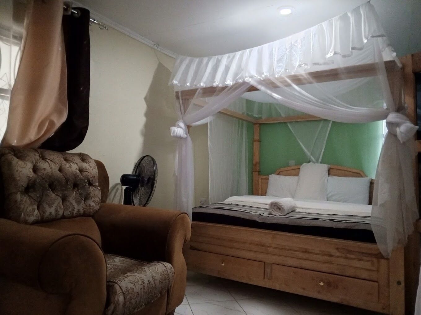 Ein Schlafzimmer mit einem Bett unter einem Moskitonetz, einem Stuhl und einem Ventilator.
