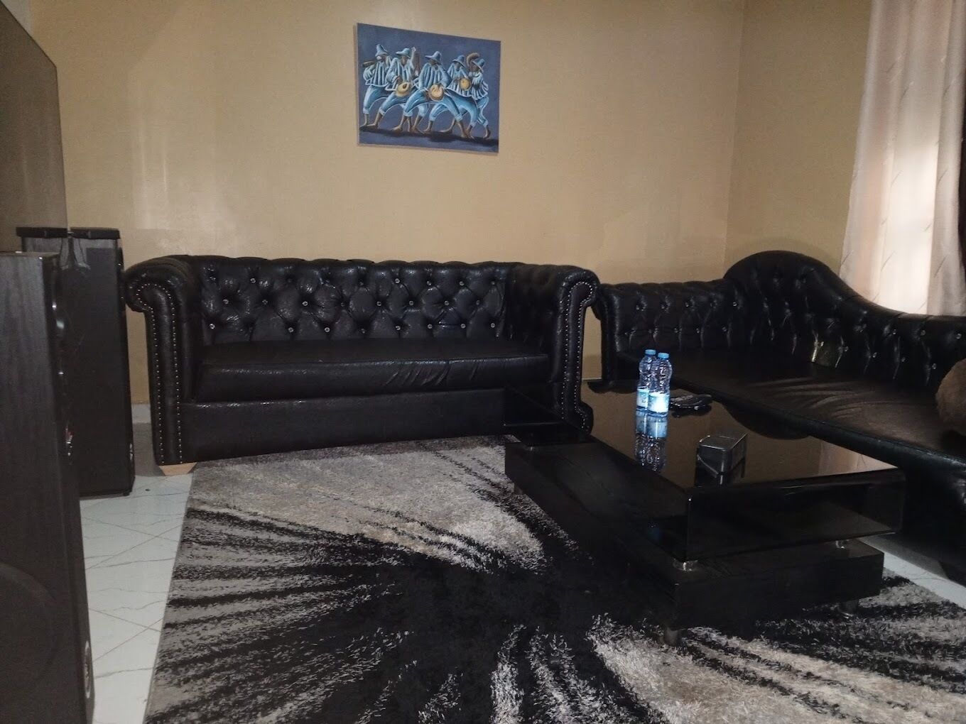 Un salon avec un canapé en cuir noir, une table basse et un tableau accroché au mur.