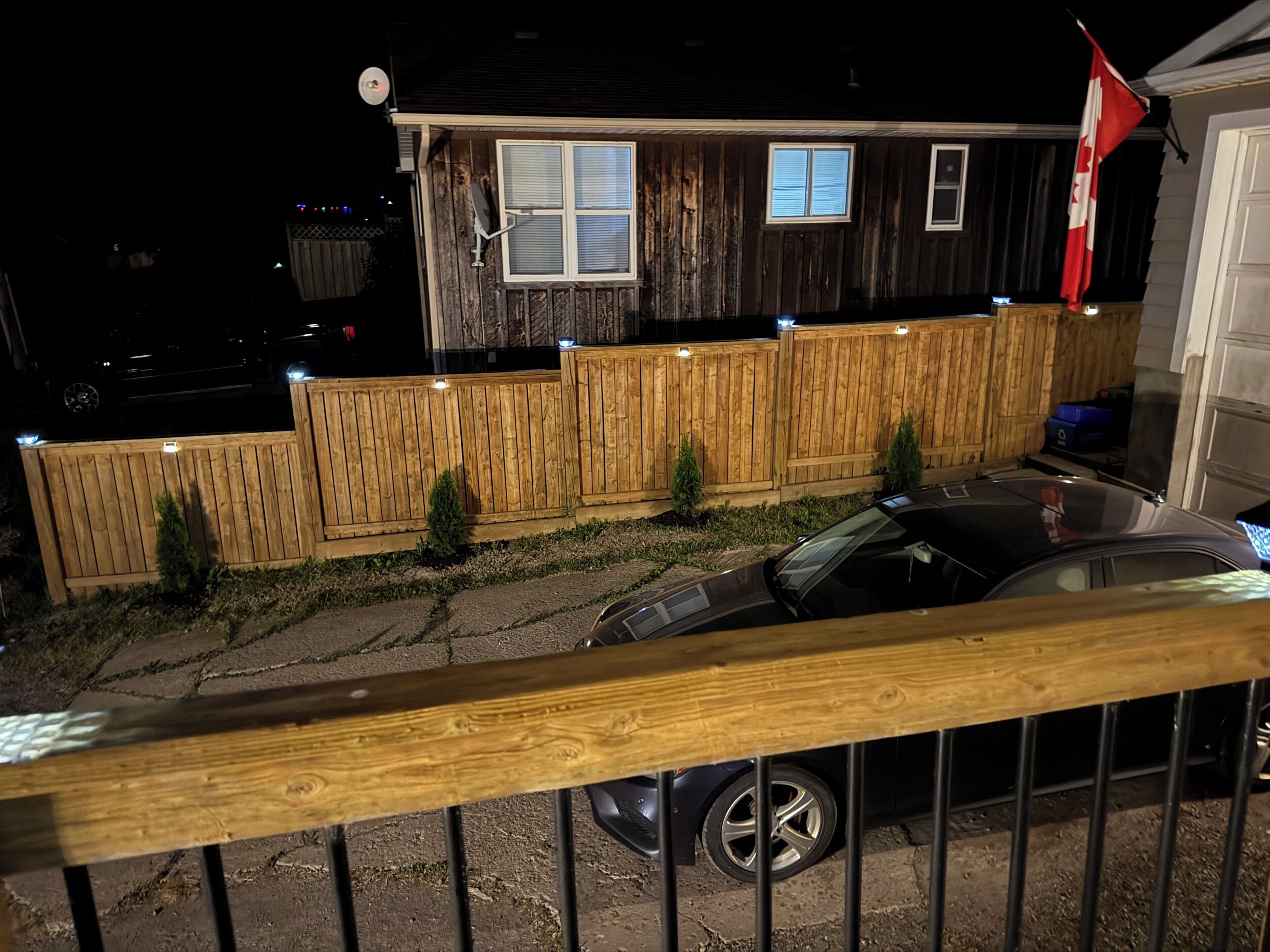 A house with a wooden fence, a flag, and a car parked in front.