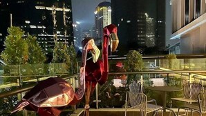 Eine Dachterrasse mit einer Metallskulptur, Stühlen und Blick auf nächtliche Stadtansichten.