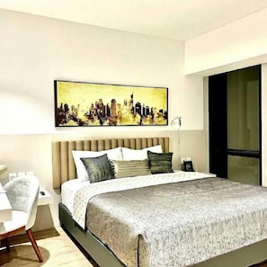 A modern hotel room with a large bed, a cityscape painting on the wall, a desk, and a chair. - The Day Residence (South Jakarta)