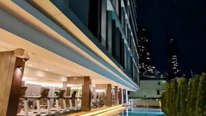 Ein modernes Hotel mit Schwimmbad, Fitnessbereich und Blick auf die nächtliche Skyline der Stadt.