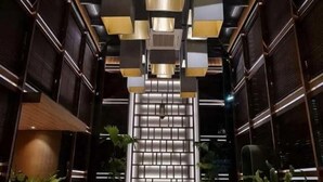 Ein modernes Interieur mit einer zentralen Treppe, dunklen Holzwänden und geometrischen Leuchten.