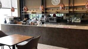Ein modernes Café-Interieur mit einer zentralen Theke, Sitzbereich und einer großen Wanduhr.