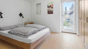 Een slaapkamer met een houten bed, een klein nachtkastje, een wandlamp en een deur naar een balkon.
