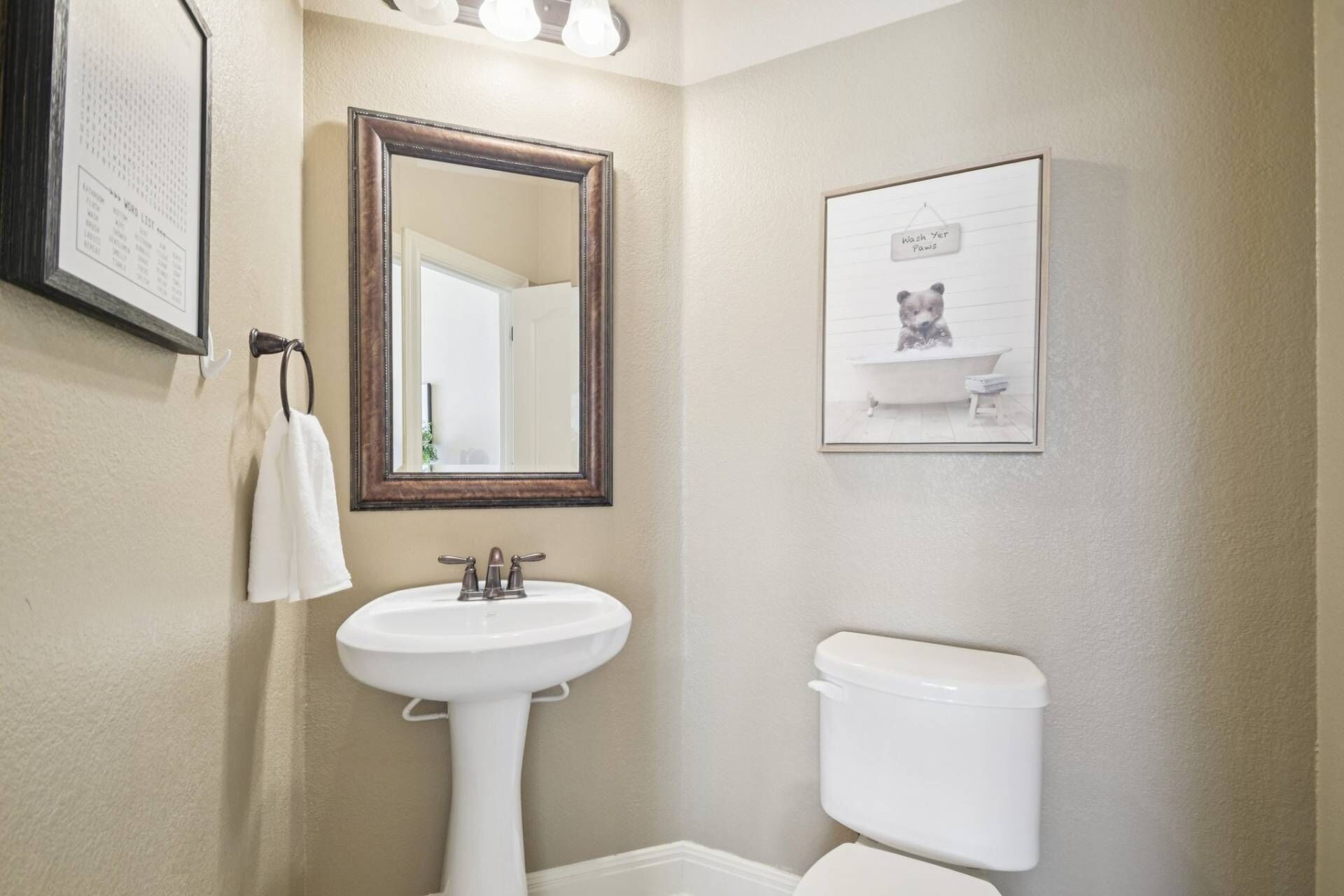 A bathroom with a pedestal sink, a toilet, a mirror, and a framed picture of a dog in a bathtub.