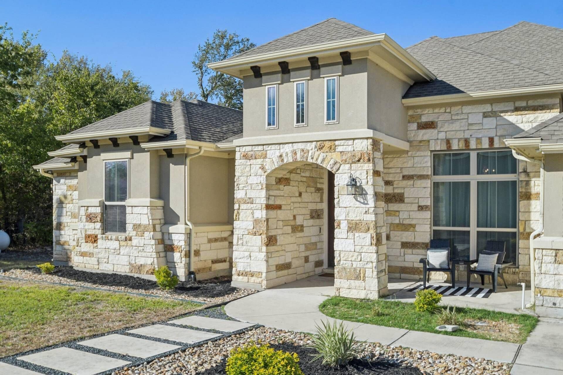 A two-story house with a stone facade, a covered porch, and a landscaped front yard.