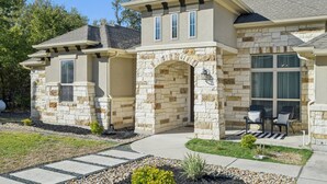 A two-story house with a stone facade, a covered porch, and a landscaped front yard. - Spacious Retreat Near Kalahari on an Acre, Updated Kitchen, Foosball, Screened Porch, Huge Backyard (Round Rock)