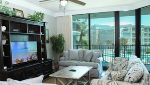 Una sala de estar con televisor, sofá, sillón y un balcón con vistas a edificios.