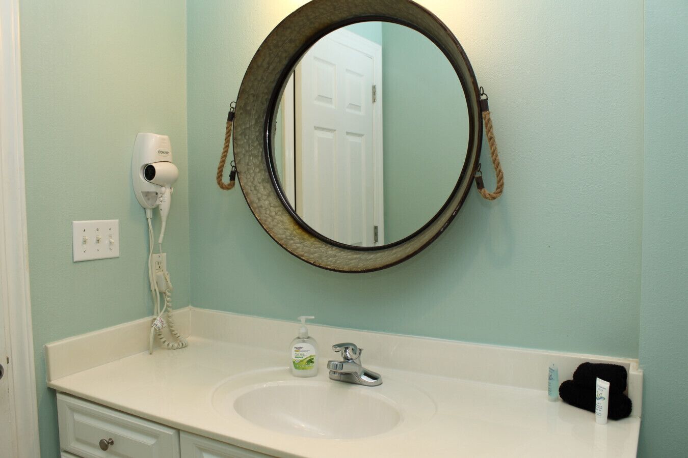 A bathroom with a round mirror, a hair dryer, a sink, and toiletries.