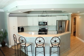 A kitchen with white cabinets, a central island with bar stools, stainless steel appliances, and a patterned backsplash.