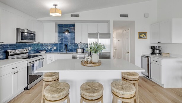 A modern kitchen with white cabinetry, a central island with stools, a microwave, stove, and refrigerator. - 2/2 Oceanview Retreat with Full Kitchen & Balcony-unit 8 (New Smyrna Beach)