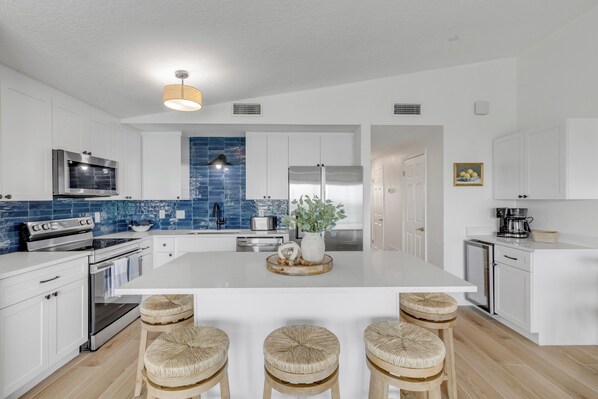 A modern kitchen with white cabinetry, a central island, bar stools, a microwave, stove, and a blue-tiled backsplash.