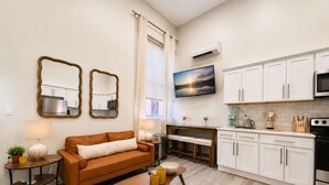A modern kitchen with white cabinets, a black oven, and a dining area with a table and chairs. - Modern Loft near Yale and Wooster Square + Parking (New Haven)