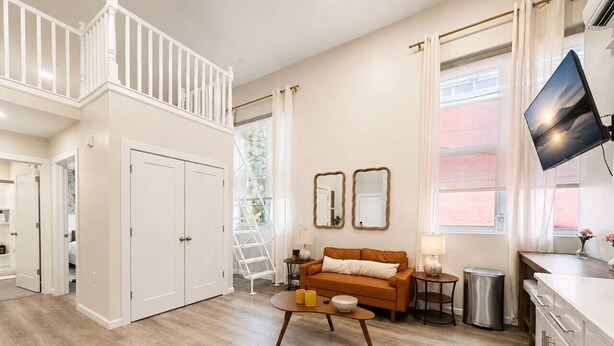 A spacious living area with a wooden floor, a sofa, a coffee table, and a TV mounted on the wall. - Modern Loft near Yale and Wooster Square + Parking (New Haven)