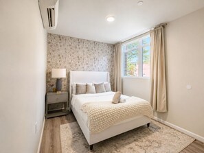 Une chambre à coucher avec un lit, une table de chevet, une lampe et une fenêtre avec des rideaux.