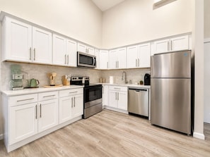 A modern kitchen with white cabinets, stainless steel appliances, and a wooden floor.