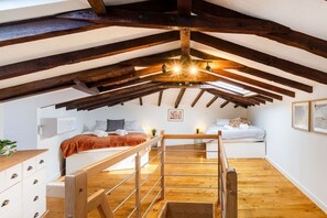 Un dormitorio con techo inclinado, vigas de madera, cama, mesitas de noche y una ventana.