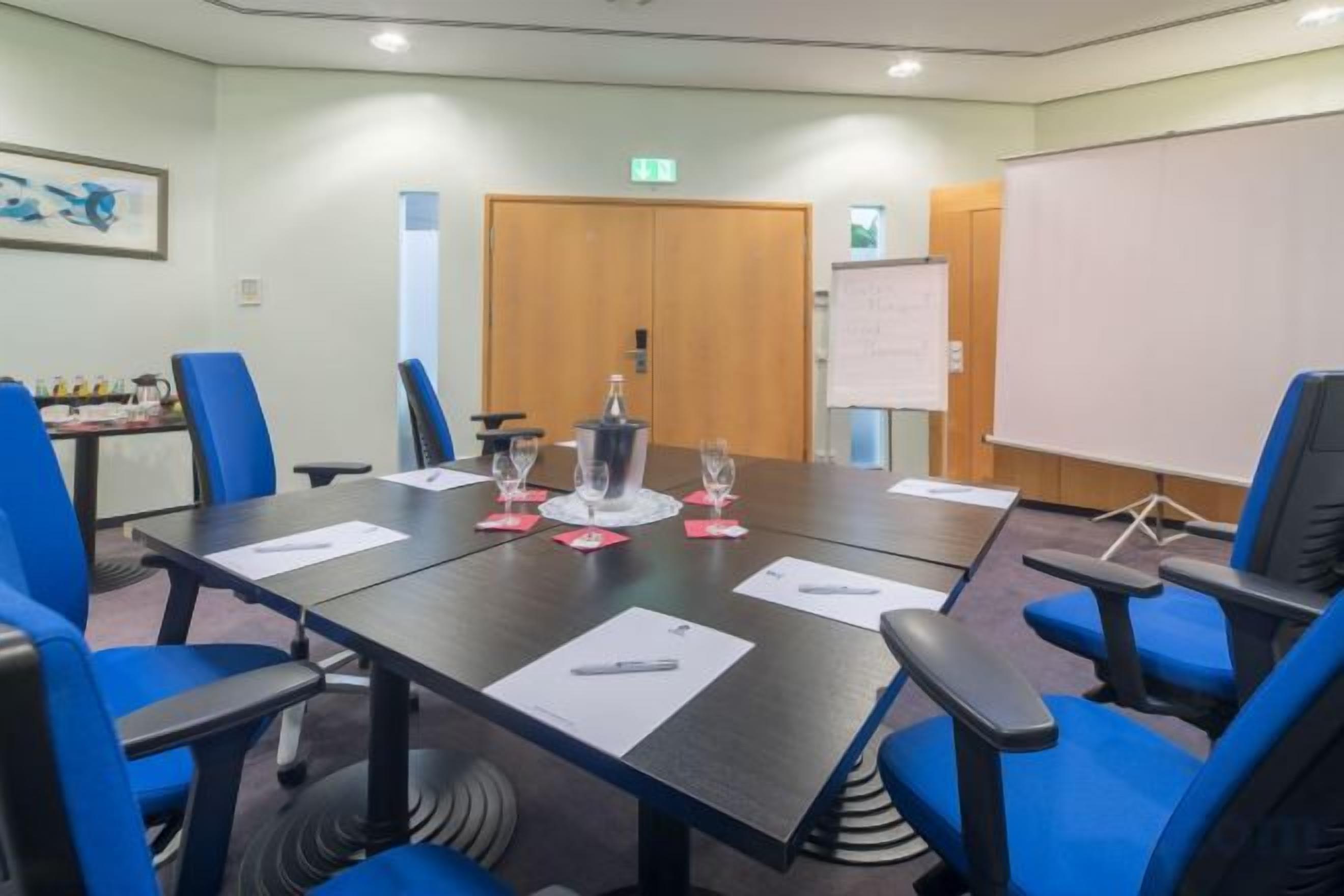 A conference room with a long table, blue chairs, a projector screen, and a whiteboard.