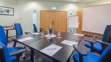 A conference room with a long table, blue chairs, a projector screen, and a whiteboard.
