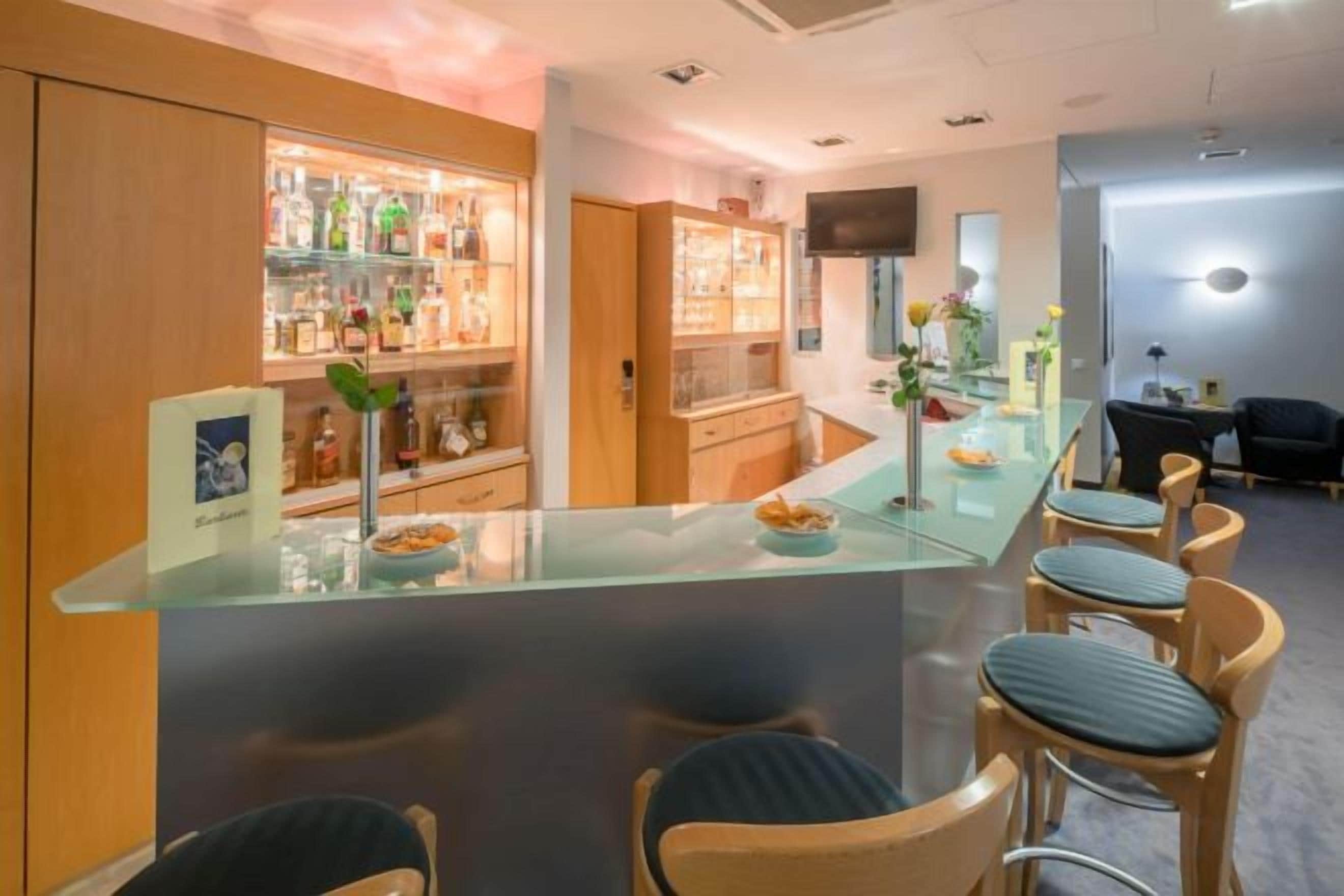 A bar area with a glass counter, bar stools, and shelves stocked with bottles.