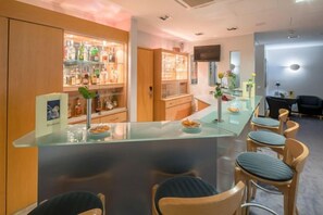 A bar area with a glass counter, bar stools, and shelves stocked with bottles. - Best Western Hotel Im Forum Muelheim (Mulheim an der Ruhr)