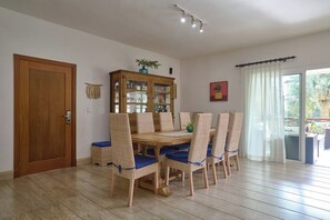 A dining area with a wooden table and wicker chairs, a wooden cabinet with glass doors, and a sliding glass door leading to an outdoor area. - 3BR~Beach~ Escape @Terrenas+Pool +Family+Balcones (El Limón)