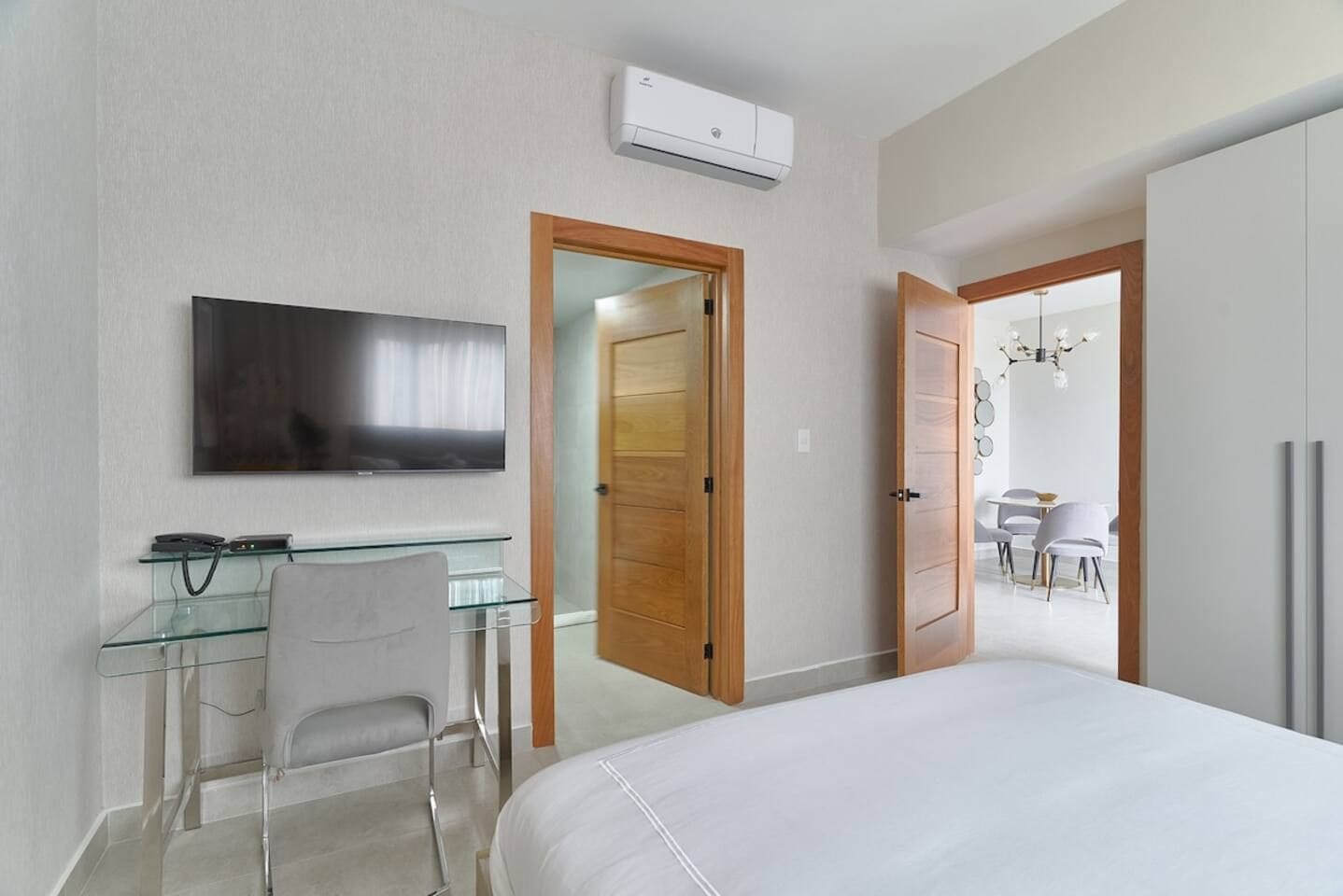 Hotelkamer met een bed, bureau met stoel, televisie en een eethoek, zichtbaar door een geopende deur.