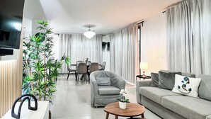 Ein modernes Wohnzimmer mit einer Couch, zwei Sesseln, einem Couchtisch und einem Essbereich mit Tisch und Stühlen.
