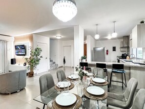 A modern living room with a glass dining table set for six, a sofa, and a TV mounted on the wall. - "The Good Life" at PGA Ocean’s 4 /GolfView/4BR Sleeps 9/Private Pool/5 Min Beach (San Pedro de Macoris)