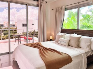 A hotel room with a bed, a nightstand, a lamp, and a view of the outdoors. - "The Good Life" at PGA Ocean’s 4 /GolfView/4BR Sleeps 9/Private Pool/5 Min Beach (San Pedro de Macoris)