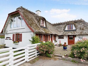 Ein traditionelles Haus mit einem Strohdach, weißen Wänden und roten Fensterläden.