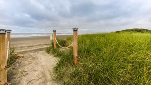 Un sentier sablonneux menant à une plage, bordée d’une clôture en treillis métallique et de lampadaires.